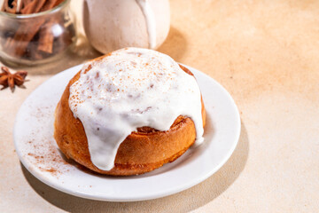 Freshly baked homemade cinnamon roll bun with vanilla topping on it, on beige background with spices, copy spaces