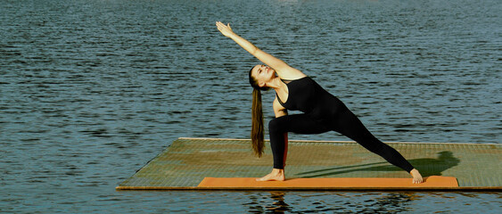 one alone young latina hispanic girl woman doing extended side extended angle yoga pose Parsvakonasana on pier of lake pond river Reflection on water surface.