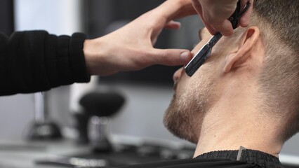 Professional barber carefully shaving client's beard, gripping straight razor with expertise while working in classic barbershop setting