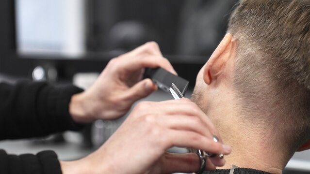 Professional barber grooming client's beard with precision, using comb and razor within stylish contemporary barbershop setting