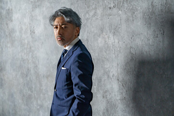 グレー背景の前でスーツ姿の男性