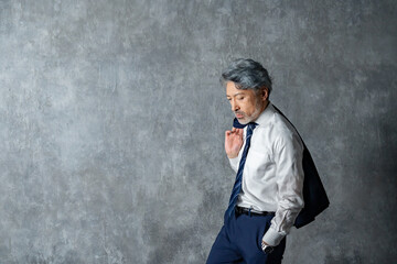 グレー背景の前でジャケットを肩にかけたポーズの男性