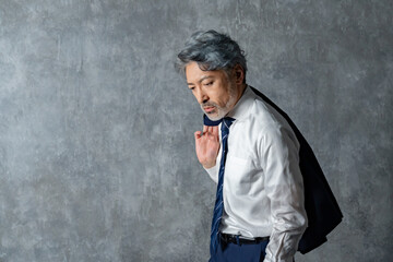 グレー背景の前でジャケットを肩にかけたポーズの男性