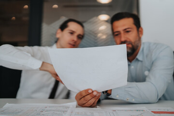 Two colleagues analyze charts and plans, sharing insights while examining a detailed paper document.
