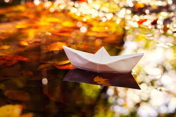 Paper Boat Floating in a Puddle Among Autumn Leaves