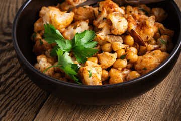Cauliflower and chickpeas curry salad on wooden table, healthy vegan food