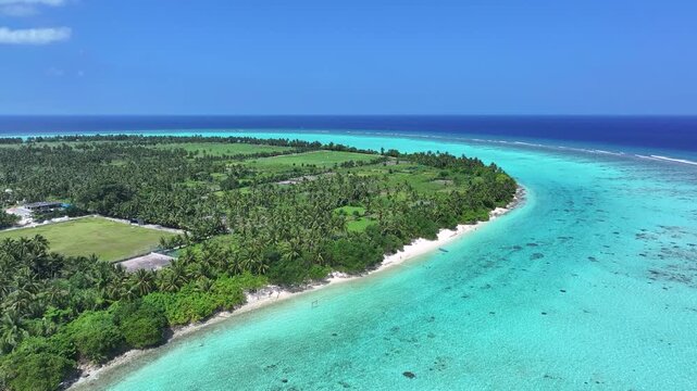 Aerial view of Thoddoo Island, a lush green island with palm trees and vibrant turquoise waters meeting the white sandy beach, Thoddoo, Alif Alif Atoll, Maldives.