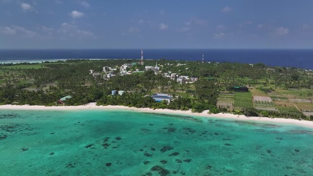 Aerial view of the Thoddoo Island, where white sands meet turquoise waters, fringed by lush green vegetation and buildings, Thoddoo, Alif Alif Atoll, Maldives.