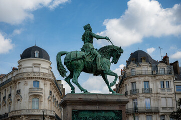 Bronze statue of Joan of Arc prominently framed between two historic buildings in Orléans, capturing the heroic figure against the urban backdrop under clear daylight.