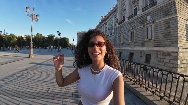 Young happy woman vlogging and gesturing in front of the royal palace of madrid. First person view of a tourist enjoying european holidays