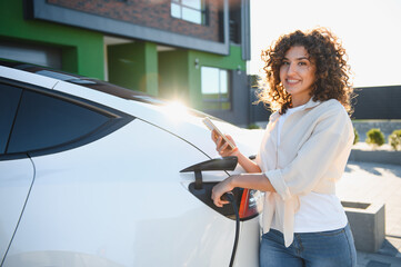 Happy woman charging electric car at home using smartphone app