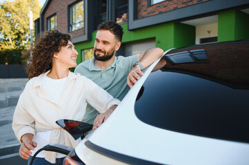 Happy couple charging electric car at home, embracing green energy and sustainable living
