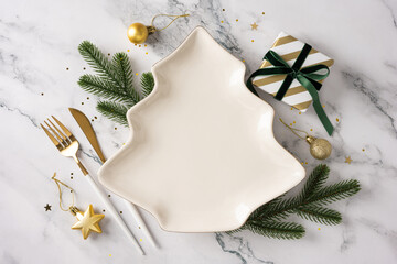 A festive table scene featuring a tree shaped plate, gold cutlery, pine sprigs, a striped gift box,...