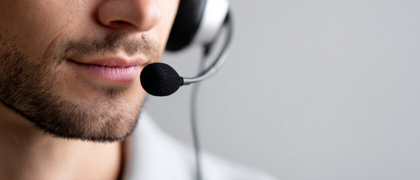 A man wearing a headset with the microphone close to his mouth, smiling slightly as he speaks into it