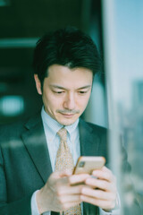Businessman in suit using smartphone by office window in natural light