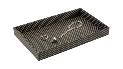 Modern carbon fiber tray elegantly displays silver skull charm bracelet and ring showcasing edgy sophistication and luxury style isolated on white or transparent png.