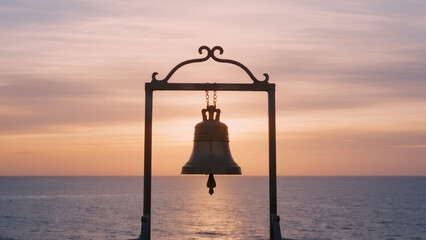  lone bell hanging from delicate frame above ocean