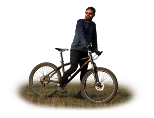 Cyclist in shorts and jersey on a modern carbon hardtail bike with an air suspension fork standing on a cliff against the background of fresh green spring forest