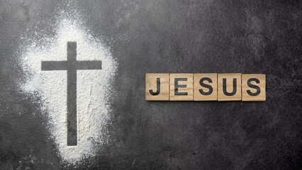 Christian cross formed by a dusting of white powder with the Jesus text on a row of wooden cubes on the table. Concept of Christianity, religious, faith, Jesus, or belief