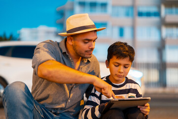 Father and son learning together with a digital tablet while sitting outside