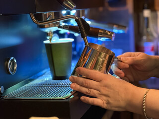 Barista preparing milk in a coffee machine for adding to coffee. Female hands are making coffee using professional metal machine in cafe. Barista is heating milk, whipping foam with frother, steam. 