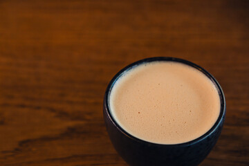 A smooth, frothy coffee served in a black ceramic mug against a wooden table backdrop.