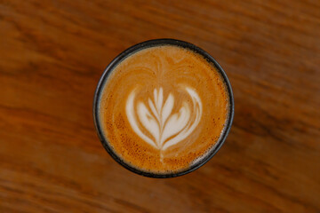 Top-down view of a cappuccino featuring intricate floral latte art on a rustic wooden surface.