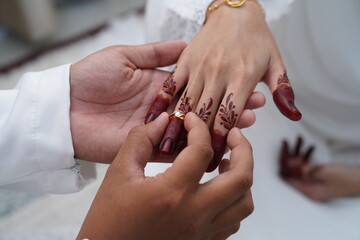 A groom gently places a wedding ring on his bride’s finger, adorned with traditional henna, during a cultural marriage ceremony. Close-up shot capturing love, tradition, and emotional connection.