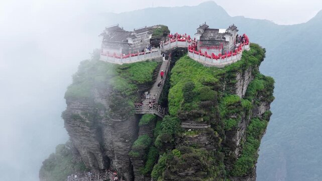 Aerial view of the Fanjingshan Temple atop a towering, cloud-shrouded peak, with winding stairs visible on the cliffside, Fanjingshan, Guizhou, China.