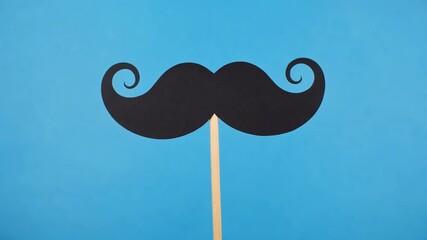 A playful black mustache on a stick against a vibrant blue background.