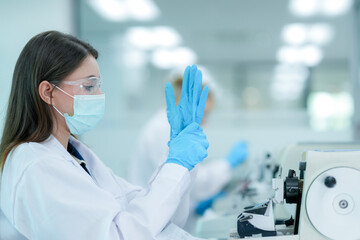A histotechnologist dons sterile nitrile gloves, following aseptic technique and safety protocols before operating a microtome to section tissue specimens in a pathology laboratory.