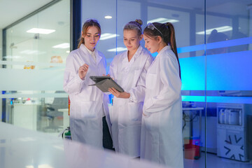 Obraz premium A group of female science students discusses their project in a modern university lab. They are working together as a team, using a tablet to analyze their experiment results.