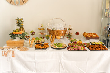 A vibrant display of a variety of appetizers and desserts is laid out on a white table. Fresh fruits, pastries, and savory dishes create an inviting atmosphere for guests at the gathering.