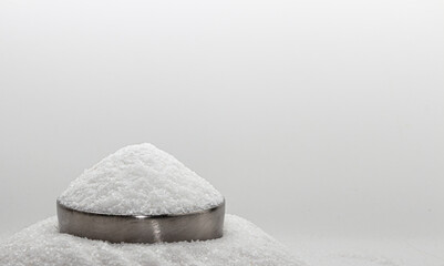 Iodated salt pile is poured into metal container in front of white background, with wooden spoon....