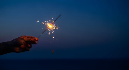 Hand holding a sparkler at dusk with a dark blue sky