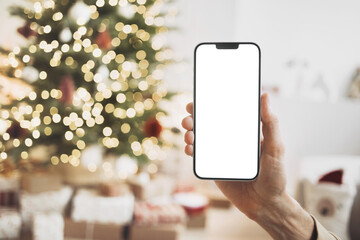 Phone mockup in hand over christmas tree, stars, gifts and decoration, Mobile phone with blank...