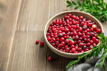 Fresh cranberries in a dark bowl on a wooden background with green branch and napkin close up.