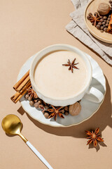 Traditional Indian masala chai tea with milk and spices in a cup on a beige background