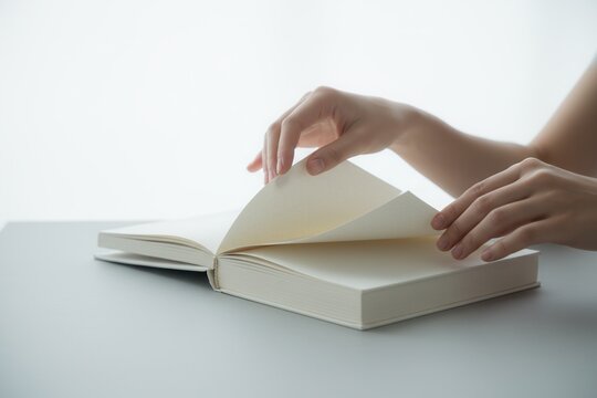 Woman's hands turning a blank page of an open book. Minimalist close-up on a white background with copy space for text