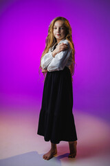Fototapeta premium Elegant child in black skirt and white blouse standing gracefully in a softly lit purple background showcasing poise and confidence