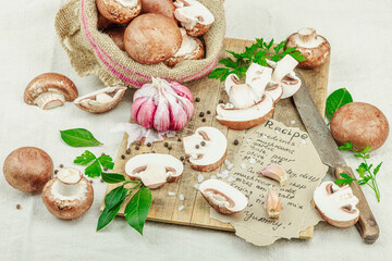 Rustic flat lay with fresh brown mushrooms, garlic, parsley, knife and handwritten recipe