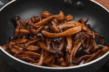 Fried Shimeji mushrooms with garlic, basil, and spices in a pan, served on a dark background