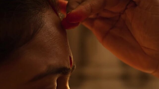 Priest applying a tilak blessing to a person's forehead in a temple.