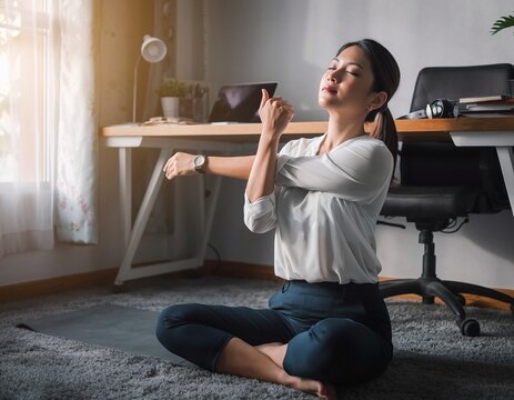 Female office worker taking a mindfulness break, stretching her arms and relaxing while sitting on the floor in a sunlit home office.