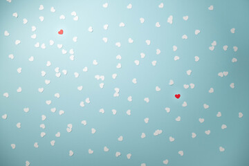 Two red among lots of white heart shape confetti on a light blue background.  Searching for the right partner concept.