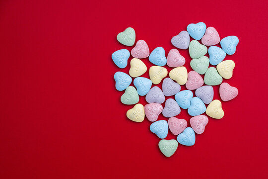 Pastel candy conversation hearts in a heart shape on a red background.  Valentine's Day background - Powered by Adobe