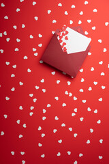 One red envelope, white card, heart-shaped confetti on red background. Valentine's Day, Mother's Day, Women's Day, Wedding, Anniversary, or Birthday.  Flat lay with copy space, vertical.