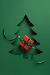 A green cutout Christmas tree card features a red gift with a dark green ribbon, creating a festive...