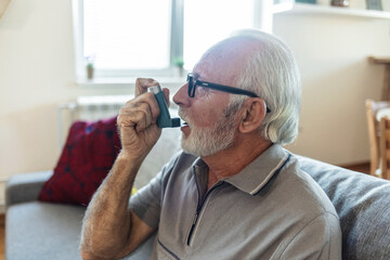 Senior man using asthma inhaler for relief an attack at home. Mature man using medical inhaler to...