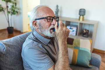 Senior man using asthma inhaler for relief an attack at home. Mature man using medical inhaler to...